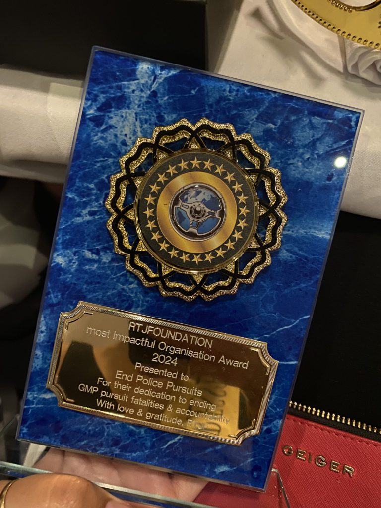 An award plaque on blue marbled backing, held in one hand. The inscription reads: RTJF Foundation, Most Impactful Organisation Award 2024, presented to End Police Pursuits for their dedication to ending GMP pursuit fatalities and accountability. With love and gratitude, RTJF.